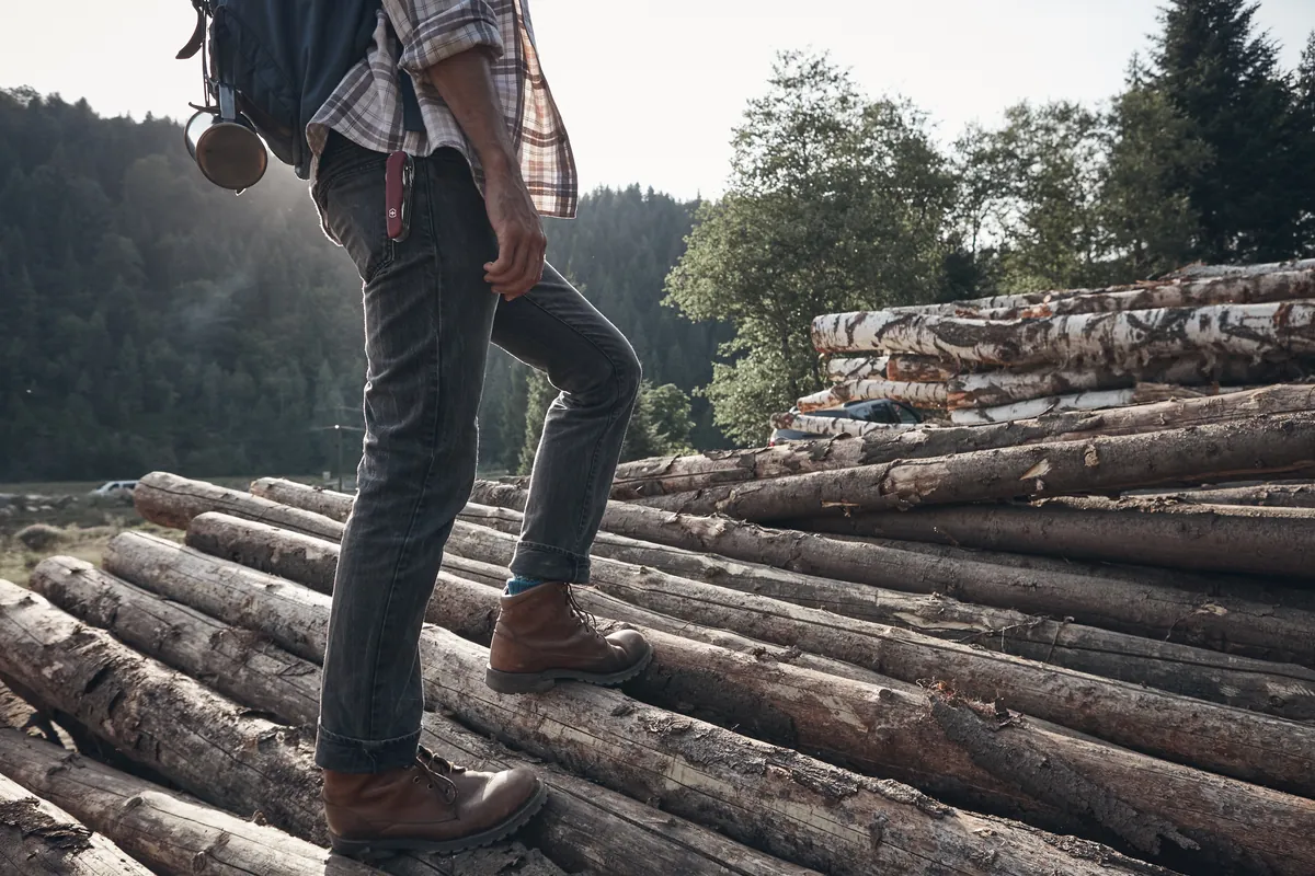 Hiker in boots walking across logs in dry woods